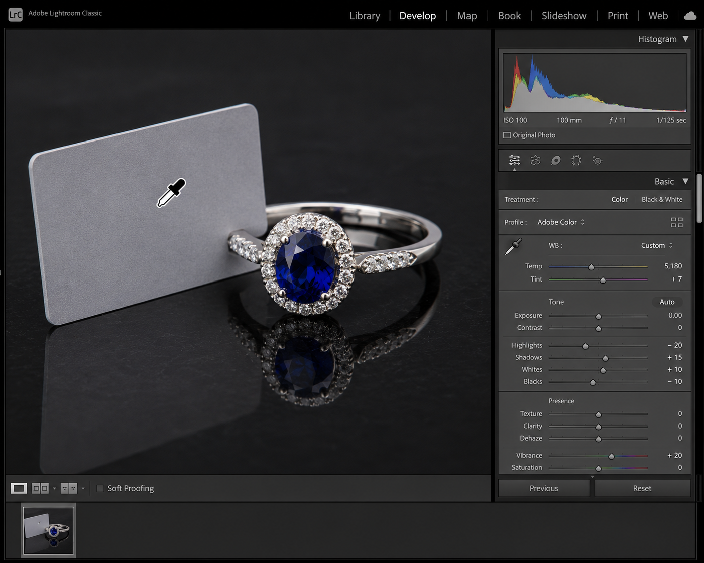 A computer screen showing a photo editing software interface using a white balance dropper tool on a grey card next to a sapphire ring