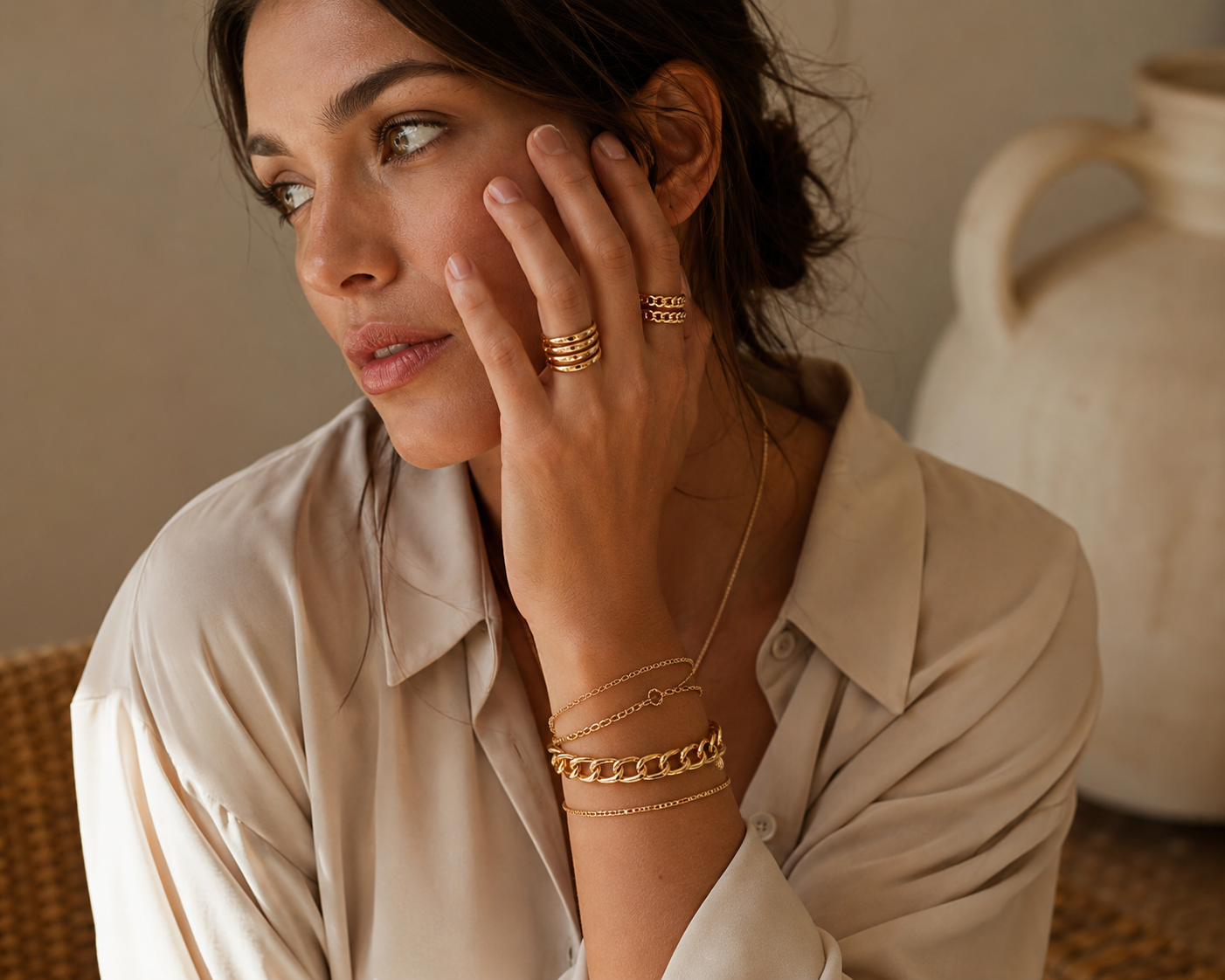 A lifestyle shot of a woman wearing stacked gold rings and bracelets, creating a warm, aspirational aesthetic