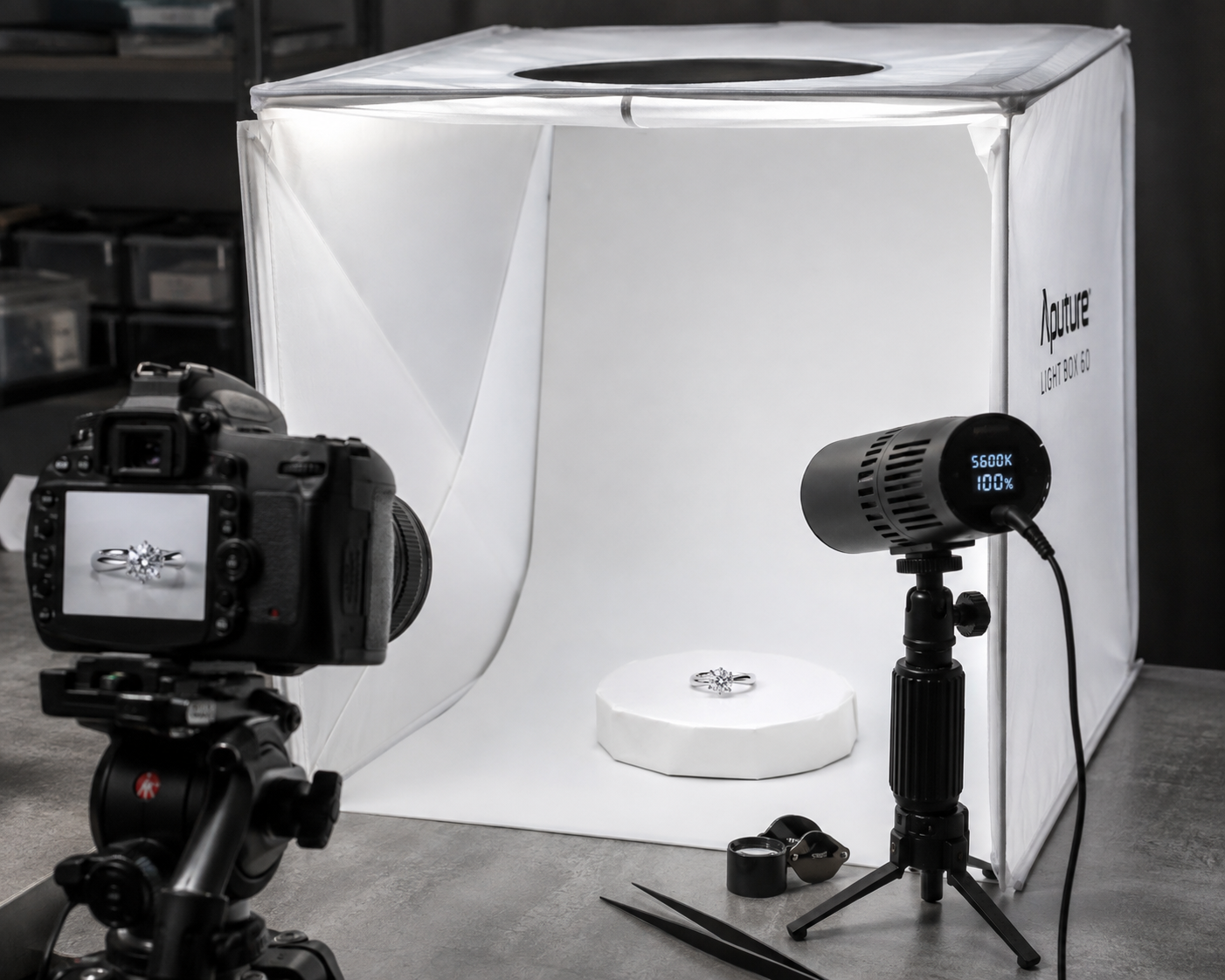 Behind-the-scenes setup showing a jewelry photography light tent with a small LED spotlight pointing directly at the diamond ring