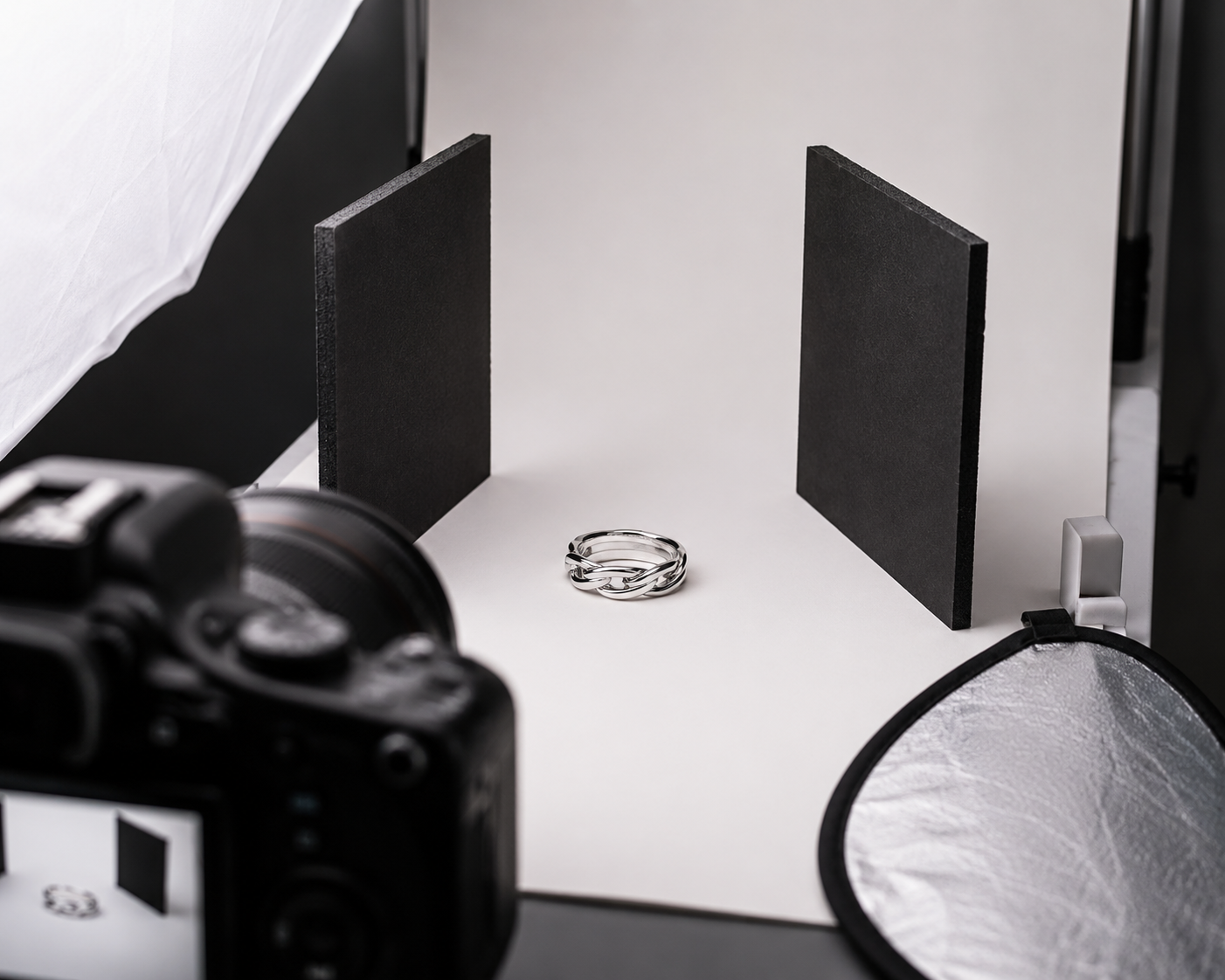 A behind-the-scenes photography setup showing small black foam boards positioned next to a silver ring to create dark edge reflections